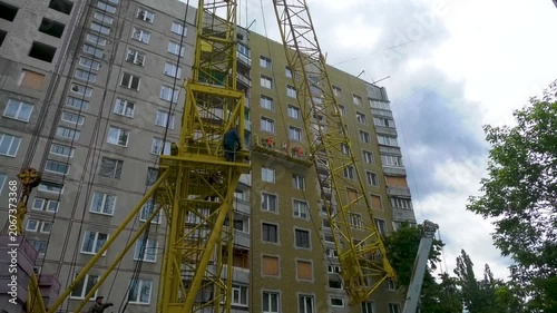 Tower crane standing beside a multi-storey residential building during renovation, repair, and thermal insulation work. Urban reconstruction project focused on energy efficiency and modernization of