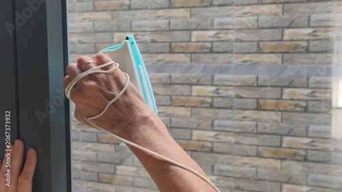 Careful hand performs window cleaning using modern magnetic tool. Safety cord protects device while smooth glass surface gets washed outside room against bright textured decorative brick wall backdrop