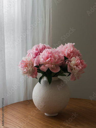 Delicate bouquet of pink peonies in a round ceramic vase on a wooden table