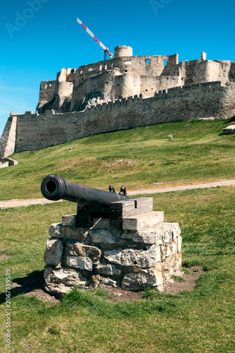 Historic cannon with Spis Castle rising above the hillside under clear blue sky in Slovakia