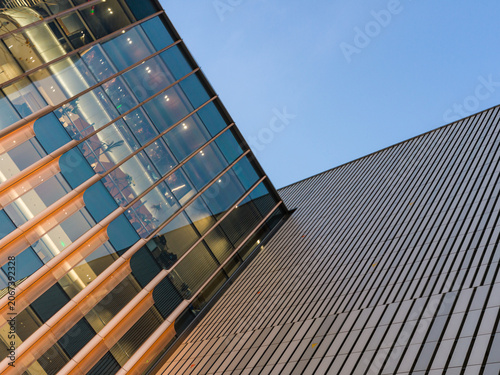 Fotografija Modern glass building reflecting sunset light next to metallic facade against sk