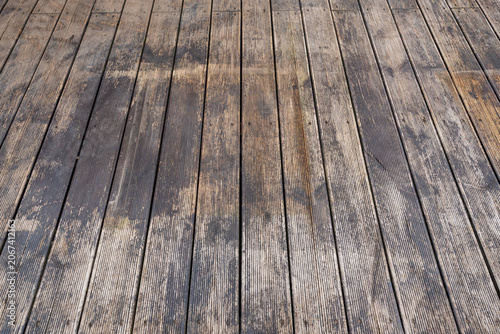 Rectangular planks run lengthwise with narrow grooves, gray to warm brown tones, dark knots, and water stains. Late day light casts angled highlights on a cleared patio.