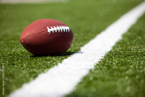 Close up of a football on a green turf field next to a white yard line