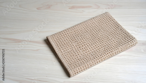 Folded beige waffle weave cotton kitchen towel on wooden table