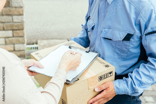 宅配便を受け取りサインをする利用者と配達員
Customer Signing for Package Delivery at Home