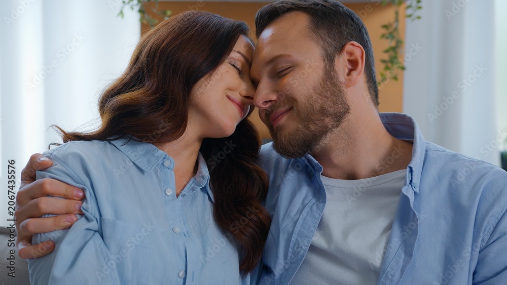 Fototapeta premium Optimistic Caucasian embracing hugging on couch smiling family cuddling embrace at home man with woman date spending time together touch faces cuddle hug anniversary valentine's day tender