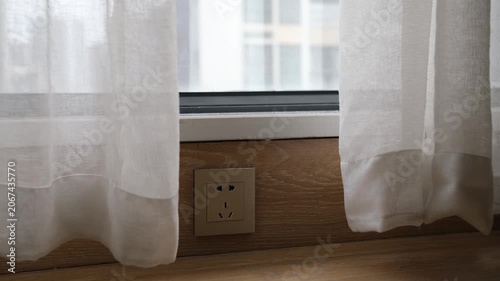 A low-mounted Chinese standard electrical power socket at skirting board level, close to the floor beneath a residential window in a contemporary Chinese apartment interior. Domestic wiring practice