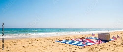Panel kuchenny z motywem Sunny beach picnic setup with american flags cooler and striped blankets on sand ocean waves and clear blue sky background perfect for summer holidays