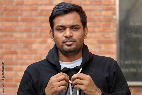 young man is outdoors wearing a black hoodie and gripping its drawstrings