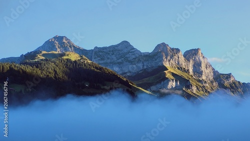 Atmospheric sunrise in the Engelberg Alps, Switzerland, featuring delicate morning mist drifting through the valleys  while the first golden sunlight illuminates the surrounding mountain peaks.