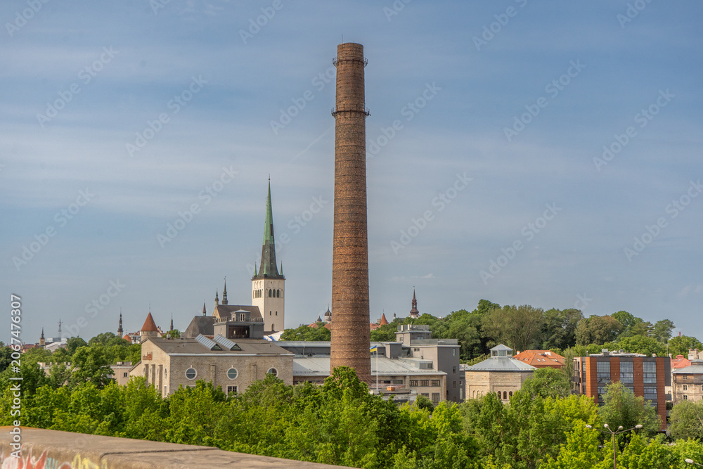 Obraz premium Historic skyline of Tallinn, Estonia, featuring a prominent industrial brick chimney rising above the city's architectural landscape and church spires.