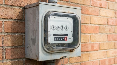 Electricity meter mounted on brick wall measuring kilowatt usage