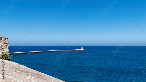 Tableau sur toile Long stone breakwater wall stretching into the deep blue sea towards a distant l