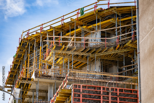 A detailed perspective of a multi story apartment building under construction featuring complex scaffolding falsework and bright yellow structural support formwork beams