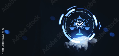Digital justice scale with glowing checkmark hovering above hand in futuristic blue interface concept technology on dark background.