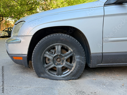 Photos Flat tire on parked silver car stands on urban street, vehicle maintenance issue, transportation disruption, roadside safety