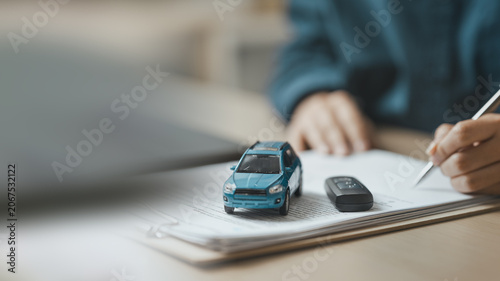 Bild auf Leinwand Businessperson signing car purchase agreement with vehicle model and key on contract documents, symbolizing auto financing, ownership transfer, and insurance planning