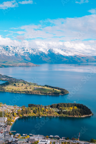 Queenstown, New Zealand: Vertical high-angle travel view over Lake Wakatipu, town center and peninsula against snow-capped Remarkables mountains.