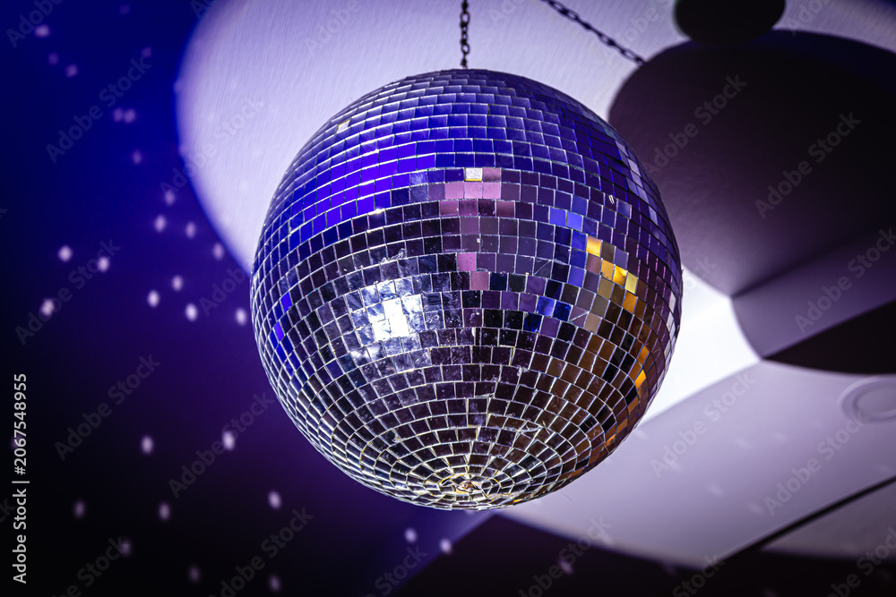 Fototapeta premium Shiny mirror disco ball with colorful reflections at nightclub. Neon sphere with bright rays, hanging on ceiling, night party background
