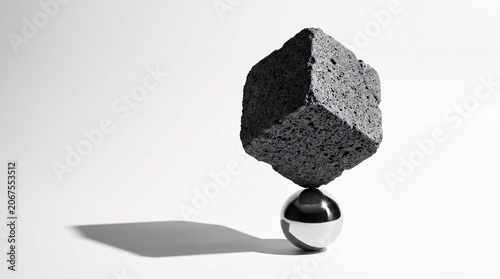 Concept of balance and stability featuring a rough black lava rock cube perfectly balanced on a polished chrome sphere