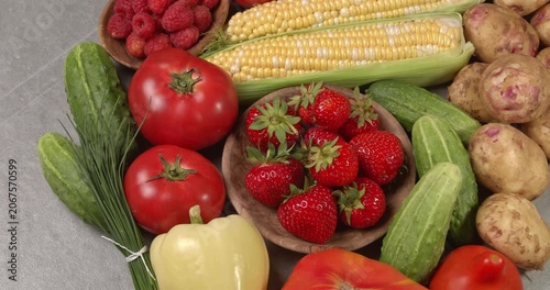 Various fresh healthy products on a gray table. Close-up footage of  corn, strawberries, cucumbers, tomatoes, green onions, potatoes, raspberries, dill, sweet peppers on a rotating table.