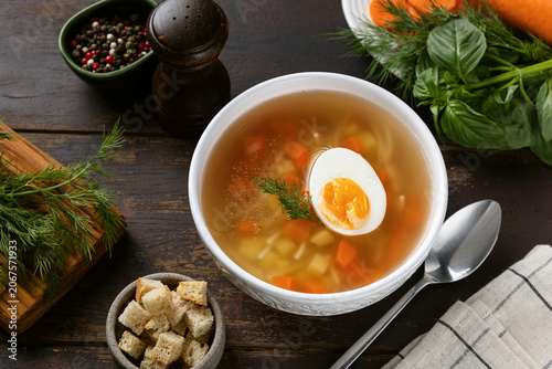 Chicken soup with vegetables and boiled egg served with croutons. Wooden background. Healthy dinner meal