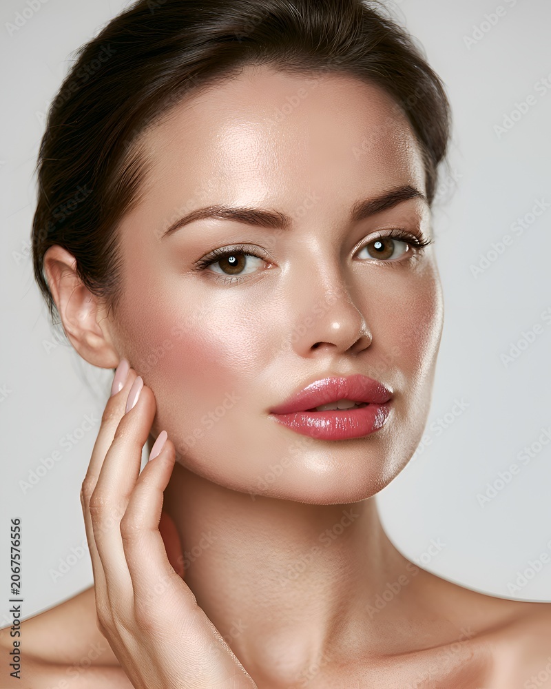 Fototapeta premium Close-up beauty portrait of a young woman with glowing healthy skin and natural makeup touching her face