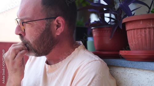 An anxious handsome man with a beard, biting nails on a terrace, making it a bad habit routine