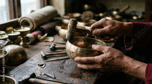 Artisan crafting a Tibetan singing bowl with hammer and tools.