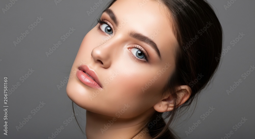 Fototapeta premium Close-up side tilt portrait of a young woman with blue eyes, professional makeup, and clean skin on a dark grey background
