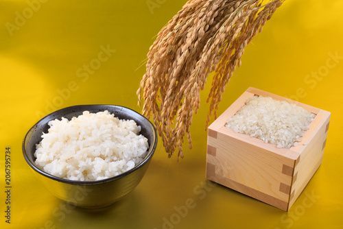 金色背景の枡に盛った米と茶碗のご飯と稲穂
