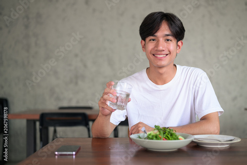 Young Asian non-binary man smiling holding glass of water looking at camera