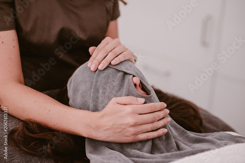 Beauty salon, a woman's face is cleaned with a special grey coloured facial towel that is wrapped around the head during a facial inside a room.