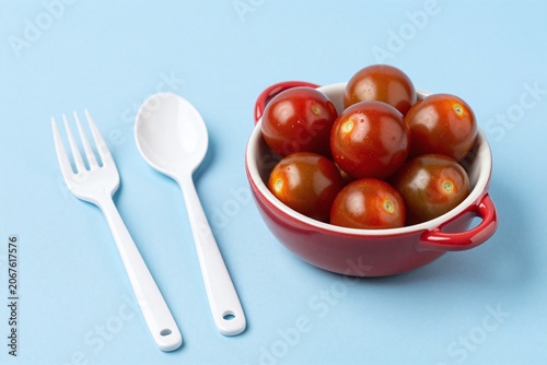 A bowl of tomatoes and a fork and spoon on a blue surface