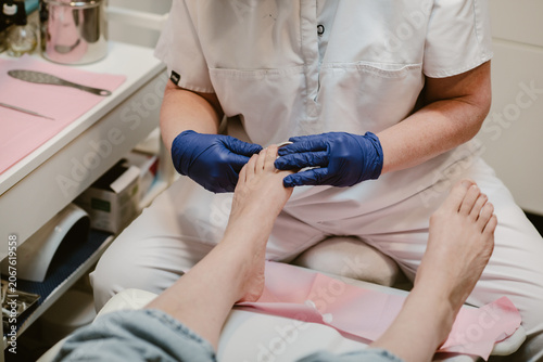 Feet care, a pedicurist wearing blue gloves for hygiene is performing foot care on a female client inside a feet spa clinic.
