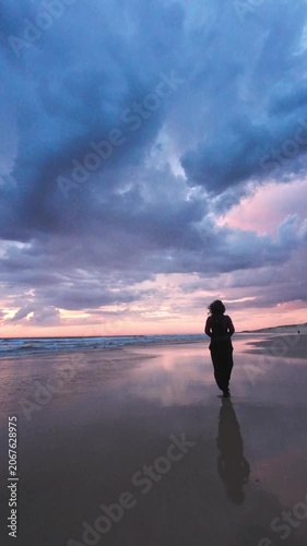 Woman walking along a large beach at sunset