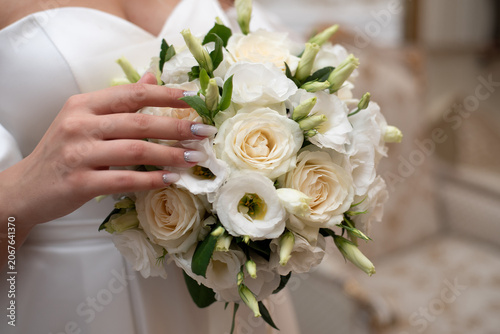 A bride holding a bouquet of pink and white roses in her hands.
