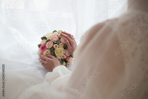 A bride holding a bouquet of pink and white roses in her hands.