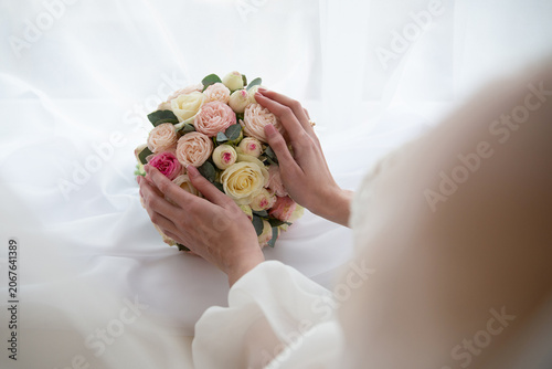 A bride holding a bouquet of pink and white roses in her hands.