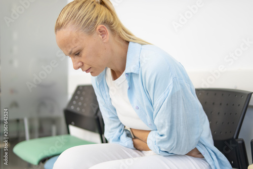 Bild auf Leinwand Woman sitting on a waiting room chair, experiencing stomach pain and nausea, han
