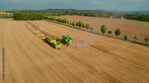 Harvester working in unison with a tractor collecting wheat on a wide open rural field during harvest time.