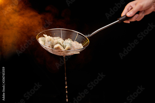 Foto Steaming boiled dumplings in wire skimmer over dark background