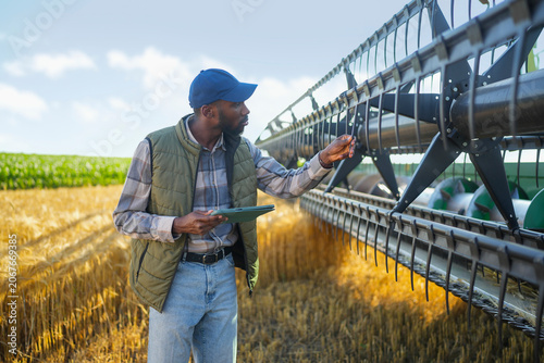 фотографія Farmer inspecting harvesting equipment while reviewing operational data on a tablet