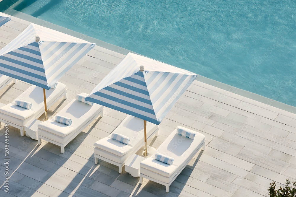 Fototapeta premium Aerial view of a luxury pool deck. Striped umbrella shades an elegant sunbed. Perfect resort vacation. Premium resort lifestyle concept. Classic striped umbrella by a luxury pool. 