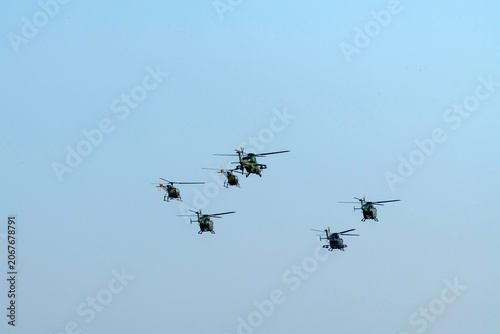 A group of silhouette helicopter squadron formation flying away on isolated blue sky