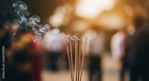 Close up of burning incense sticks releasing fragrant smoke during a spiritual ceremony with soft sunlight