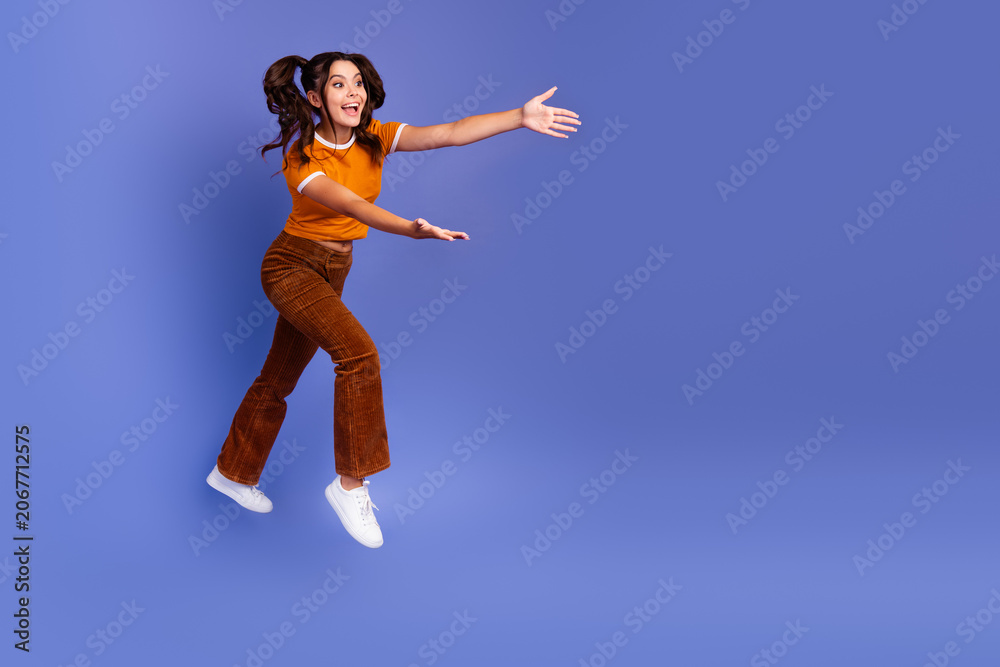 Naklejka premium Happy young girl jumps in orange top and brown pants against violet background for lifestyle fashion promotion