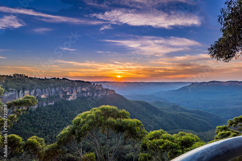 A vibrant sunset illuminates the iconic Three Sisters rock formation in the Blue Mountains National Park of Australia.