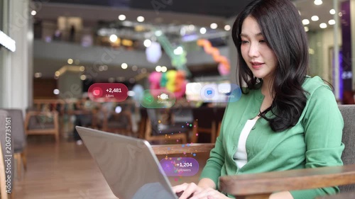 Beautiful young Asian woman content creator working on a laptop at a cafe with floating social media notification icons like likes, comments, shares, Successful online engagement and digital marketing