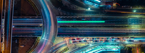 Aerial view of modern highway interchange with dynamic light trails at night, symbolizing smart city infrastructure, sustainable transportation, EV mobility, ESG investment, and future business growth